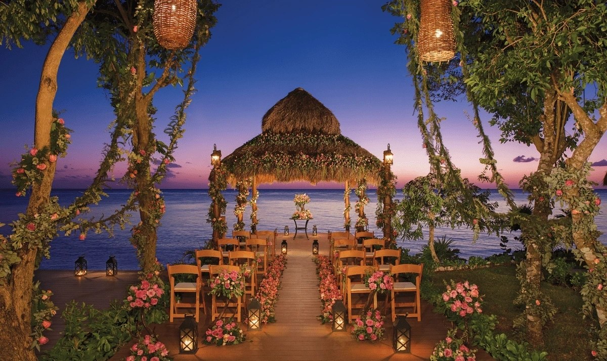 Beachfront wedding gazebo at sunset with lanterns and a floral arch