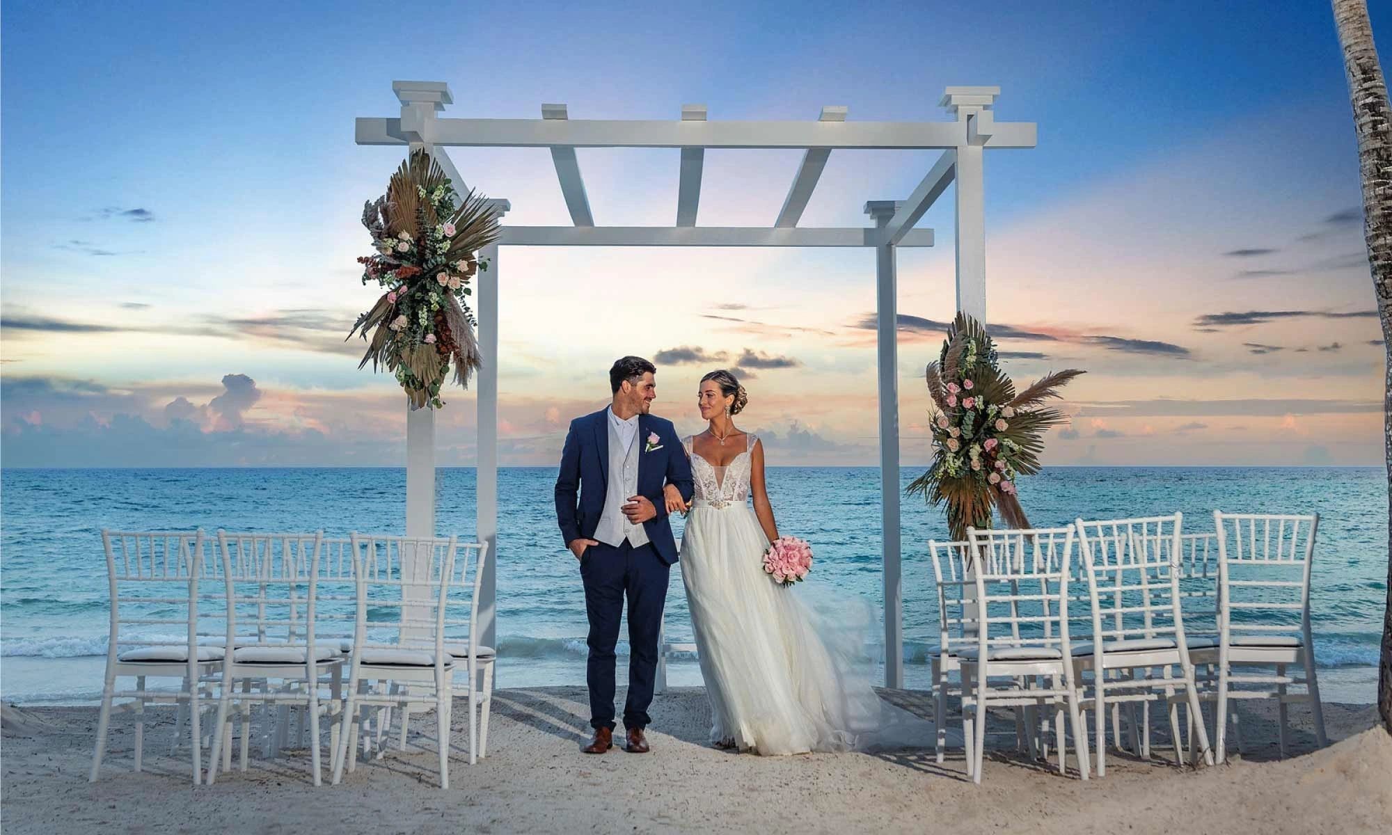 Newlyweds beneath a white arch overlooking the ocean